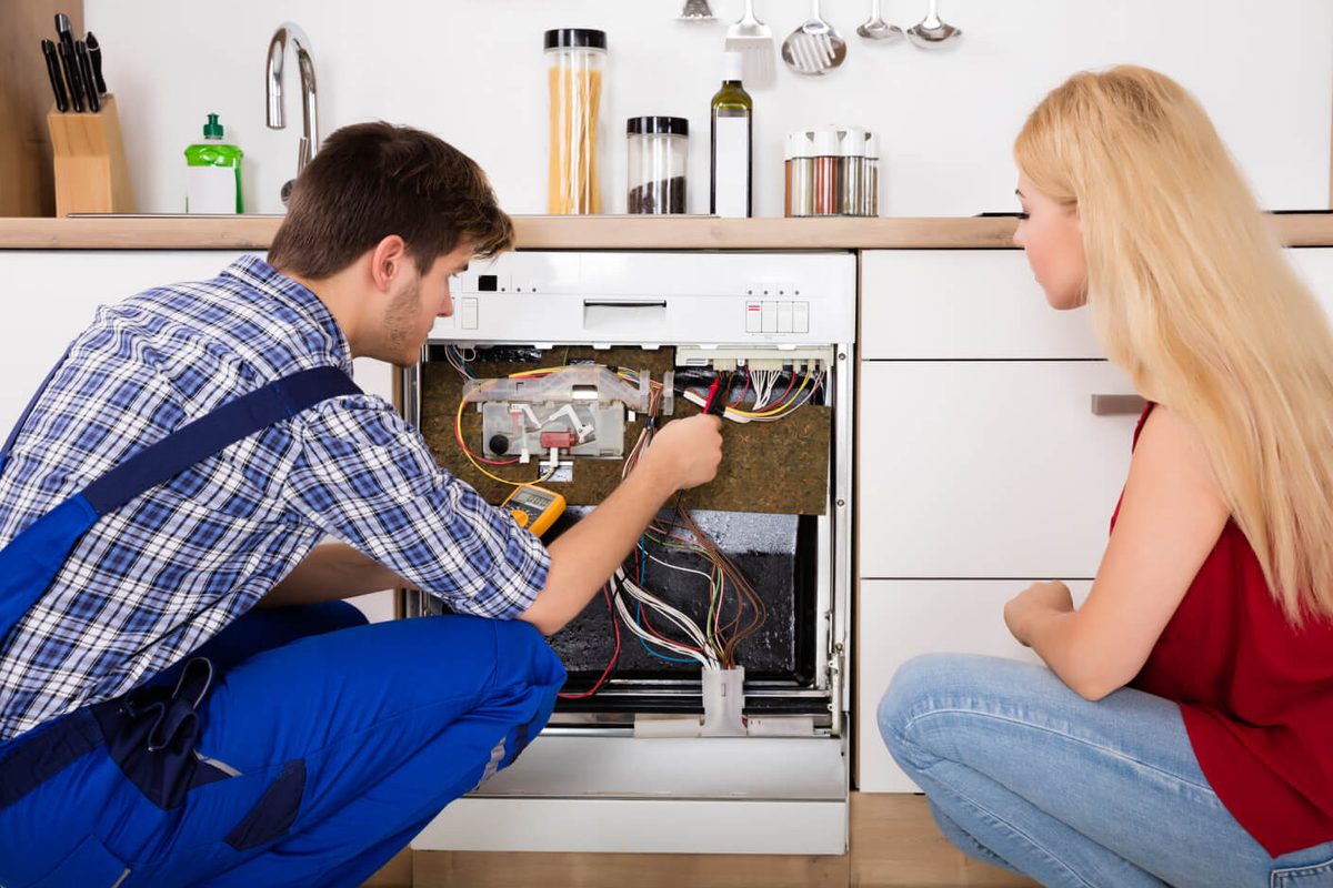Technician diagnosing a built-in dishwasher's wiring while the homeowner looks on